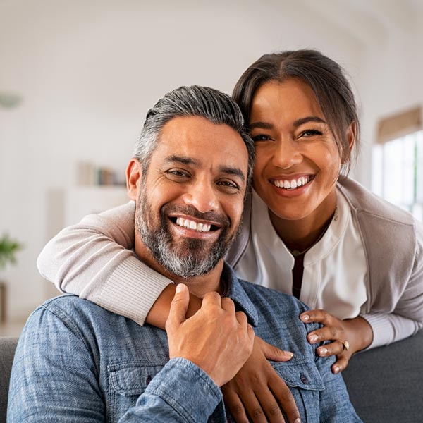 Portrait of multiethnic couple embracing and looking at camera sitting on sofa.